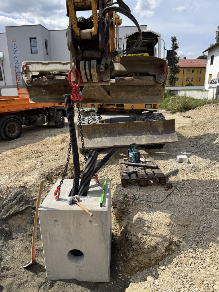 Bagger beim Setzen eines Betonfertigfundaments mit schwarzen Kabelschutzrohren für einen 300-kW-MegaCharger.
