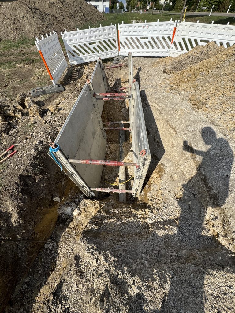 Blick in einen mit Verbauplatten und Querstreben gesicherten Leitungsgraben mit freigelegter Hauptwasserleitung.